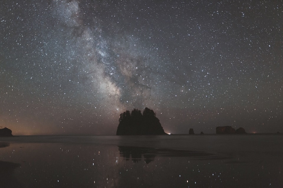 Un ciel étoilé au-dessus d’une mer calme, avec la silhouette d’une petite île.
