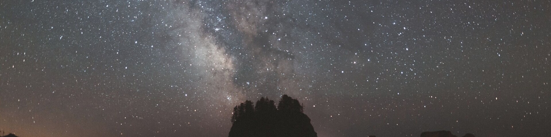 Cielo estrellado sobre un mar tranquilo, con el perfil de una pequeña isla.
