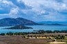 Paesaggio costiero con montagne, un lago e un parco alberato.