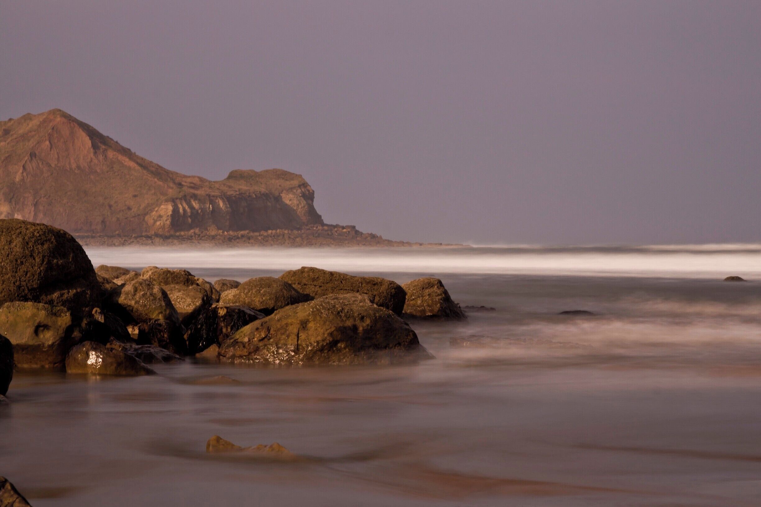 A rocky shoreline with large boulders and a distant mountain range.