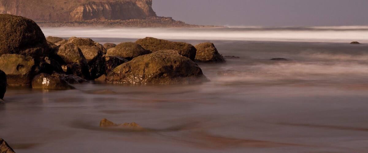 A rocky shoreline with large boulders and a distant mountain range.