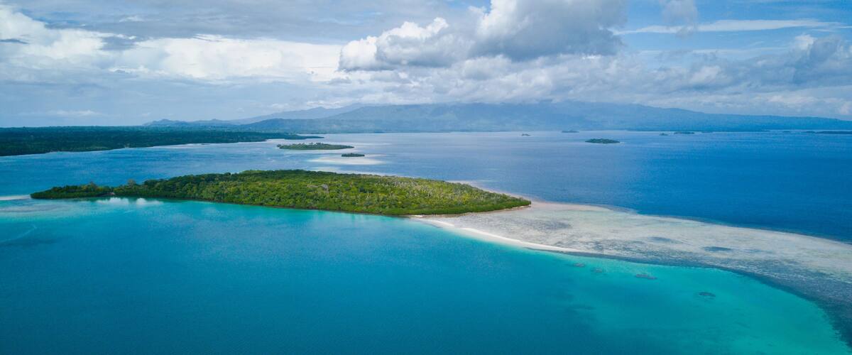 A turquoise sea with a small island and a sandy beach.