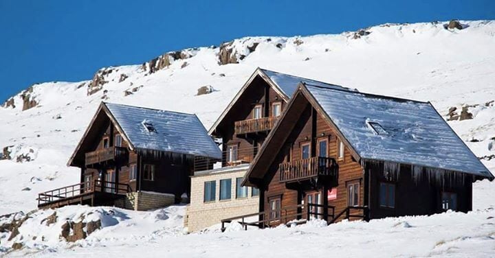Two wooden cabins with steep roofs on a snowy mountain.