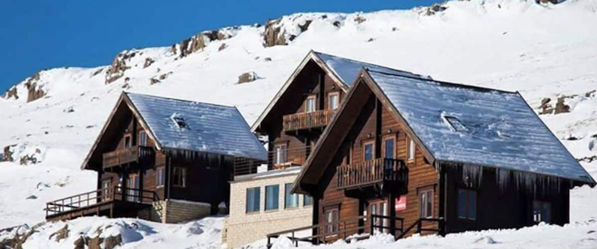 Two wooden cabins with steep roofs on a snowy mountain.