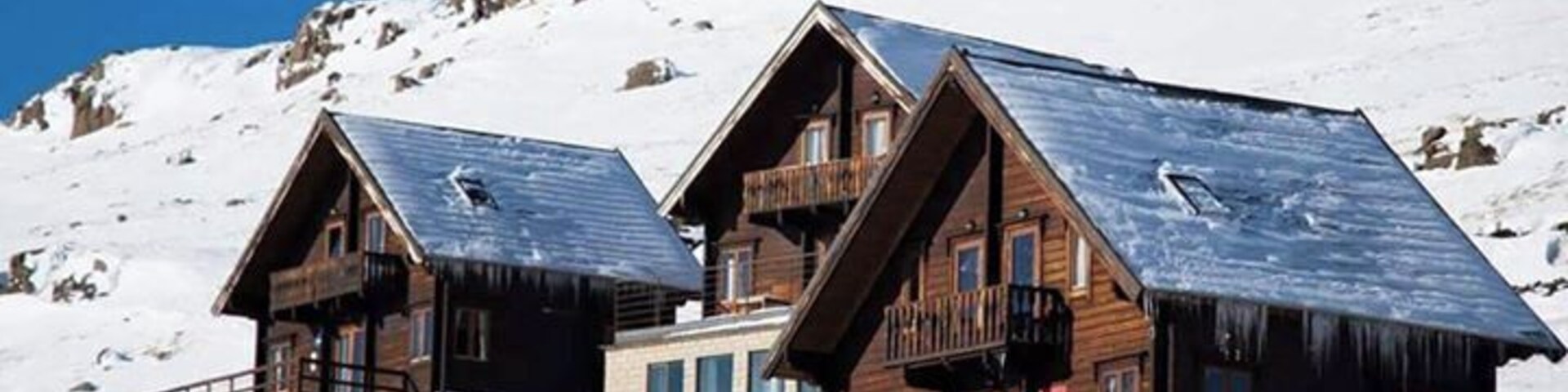 Two wooden cabins with steep roofs on a snowy mountain.