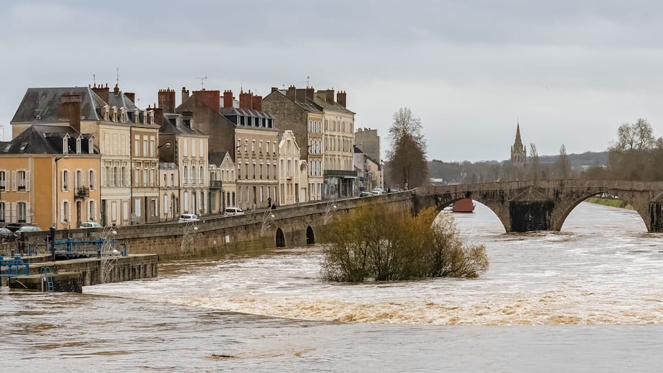 A flooded river with a stone bridge and historic buildings along the riverbank.