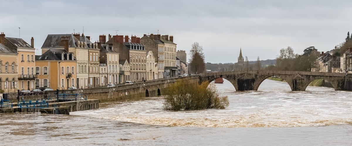 A flooded river with a stone bridge and historic buildings along the riverbank.