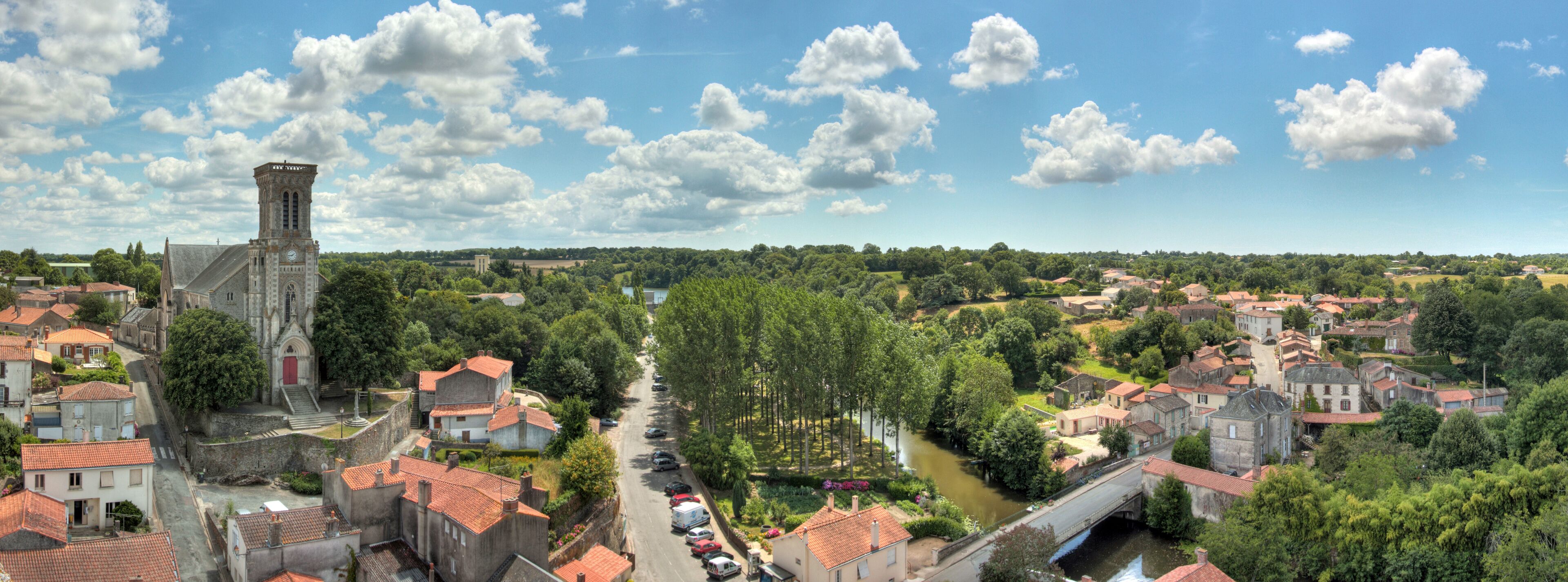 A town with a prominent church tower, a river, and a bridge.