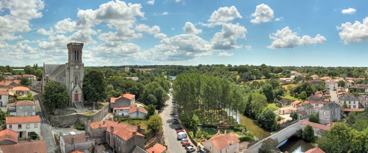 A town with a prominent church tower, a river, and a bridge.