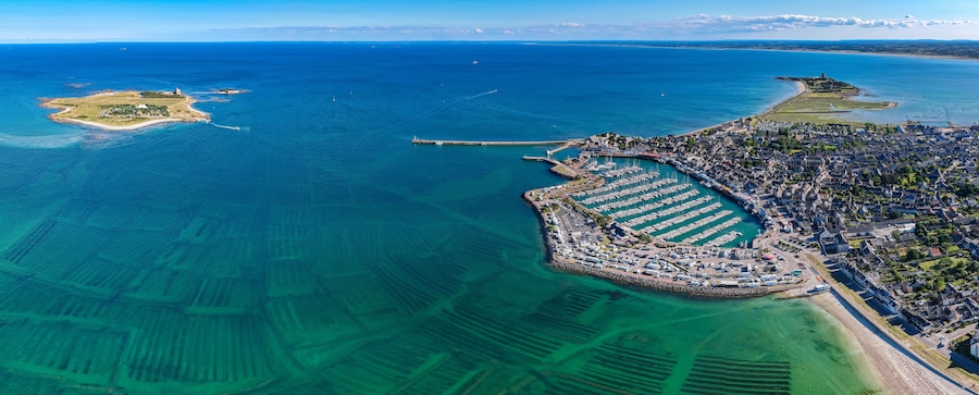 An aerial view of a coastal town with a marina, a lighthouse, and a small island.
