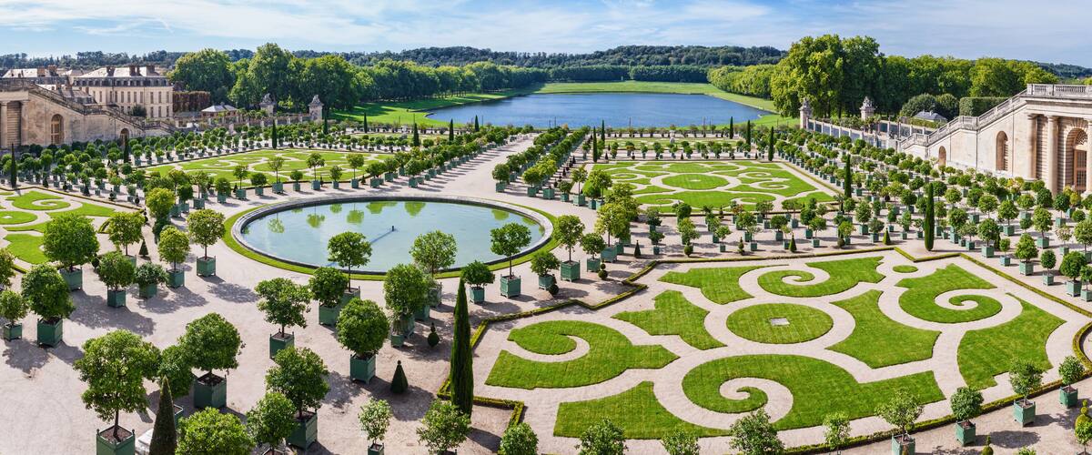 A formal garden with geometric patterns, a central pond, and surrounding buildings.