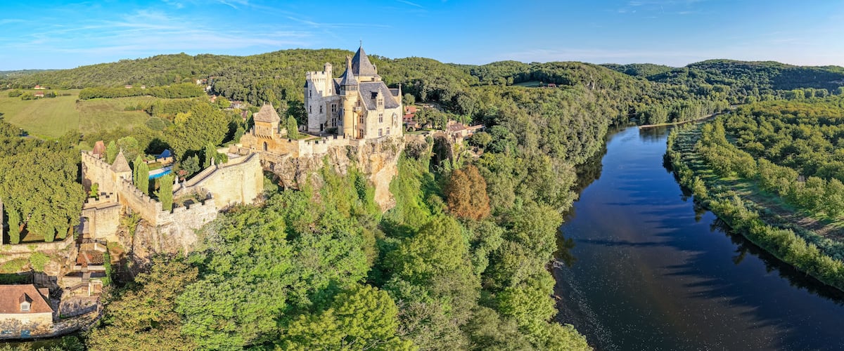 A castle on a hill overlooking a river surrounded by dense forest.