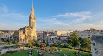 A cathedral with a tall spire, surrounded by a cityscape with buildings and a park with people.