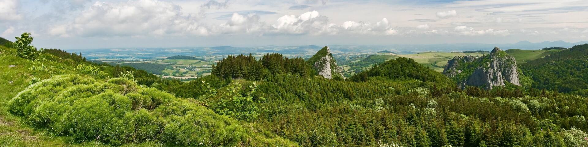 A lush green landscape with rolling hills, dense forests, and rocky outcrops under a partly cloudy sky.