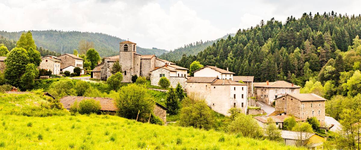 A village with stone buildings nestled in a lush green valley surrounded by forested hills.