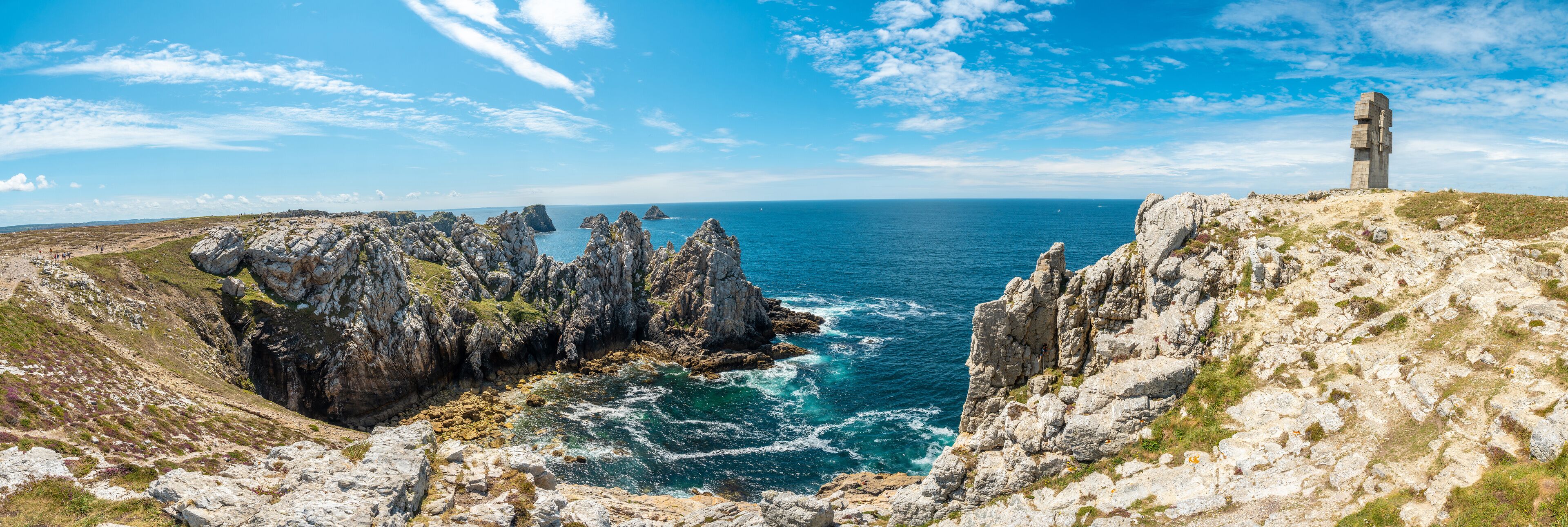 A coastal landscape with rocky cliffs, a sea view, and a tall stone monument.