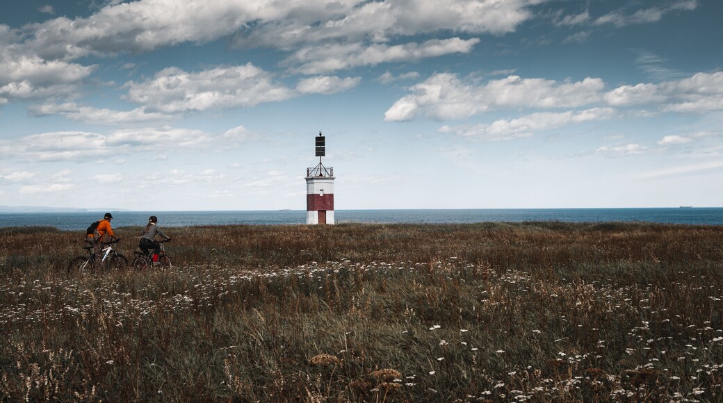 A girl and a lonely red-white lighthouse in an autumn field on the shores of the Okhotsk Sea in the north of the Khabarovsk Territory of Russia