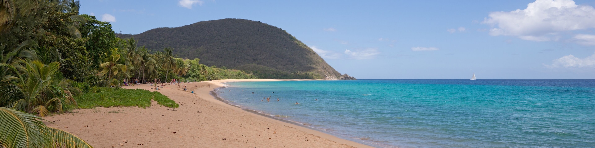 A beach with clear turquoise water, a sandy shore, and a mountain in the background.