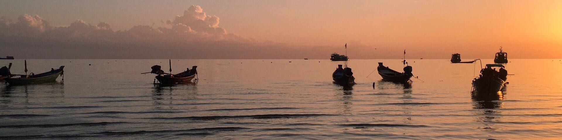 A calm sea at sunset with several boats anchored.