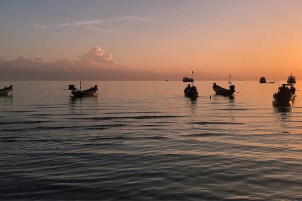 Ein ruhiges Meer bei Sonnenuntergang mit mehreren vor Anker liegenden Booten.