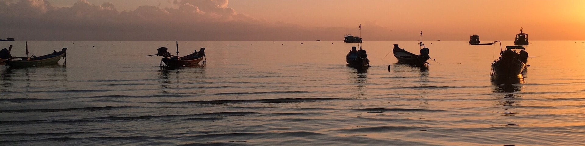 Mar tranquila al atardecer con varias embarcaciones ancladas.