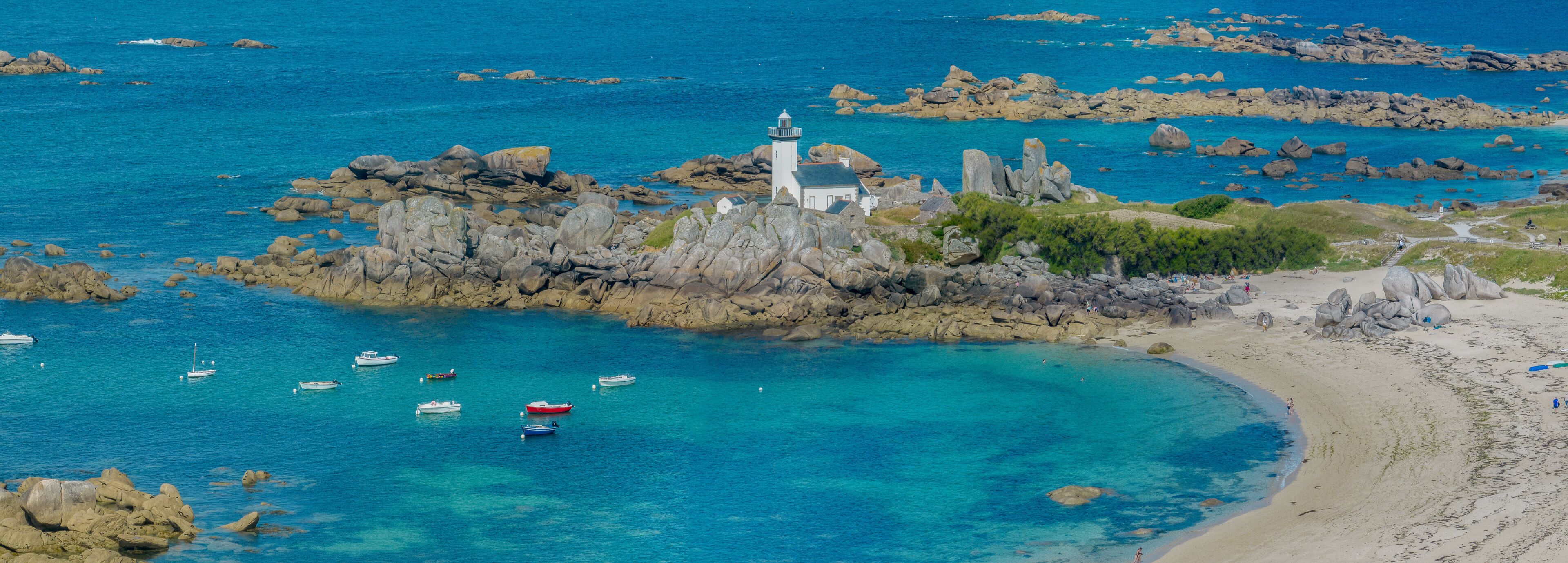 A coastal landscape with a lighthouse, rocky outcrops, clear turquoise waters, and a sandy beach.