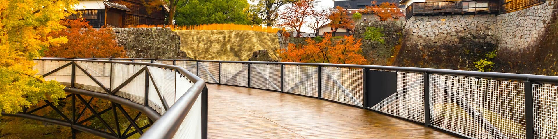 A wooden bridge leading to a traditional Japanese castle with autumn foliage.