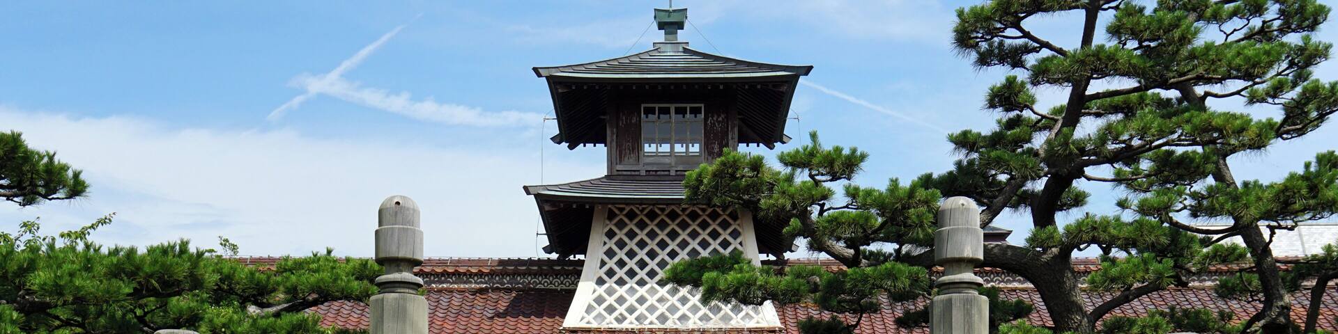 A traditional Japanese gate with a red door, leading to a building with a pagoda-style roof.