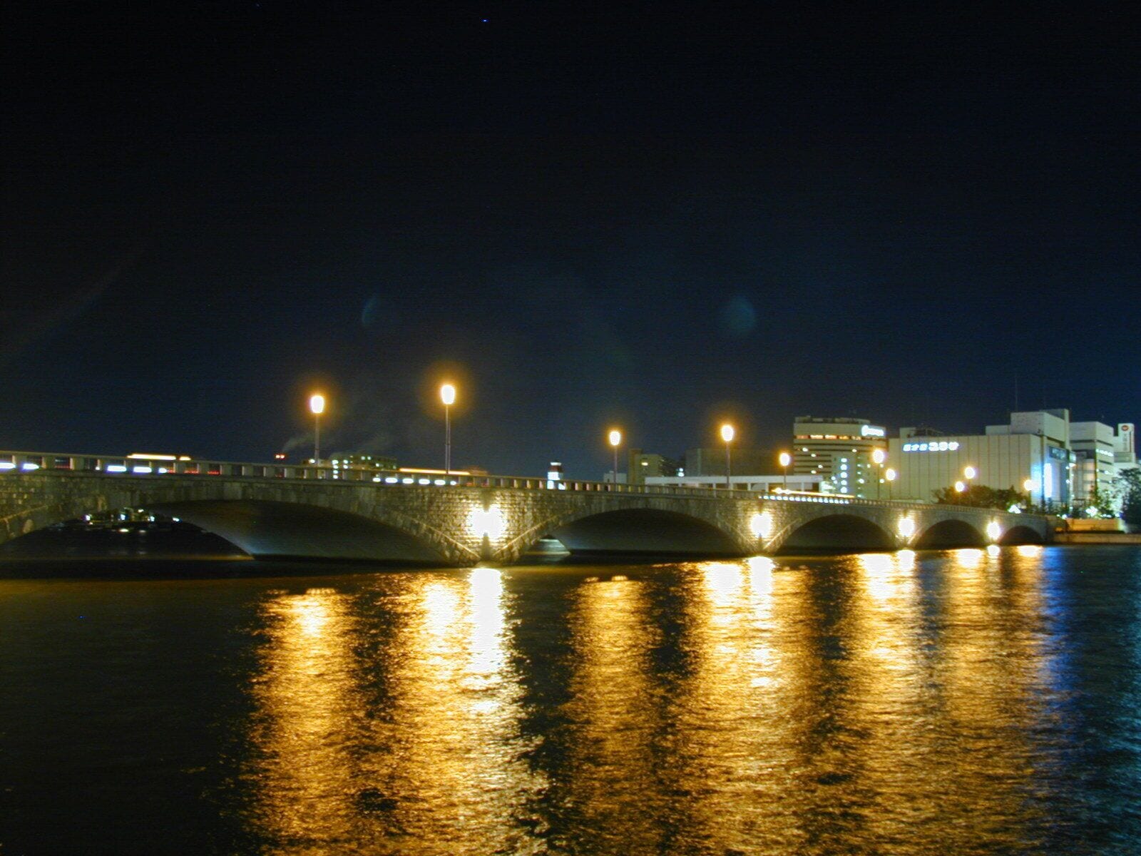 Un puente de piedra con luces que se reflejan en el agua de noche.