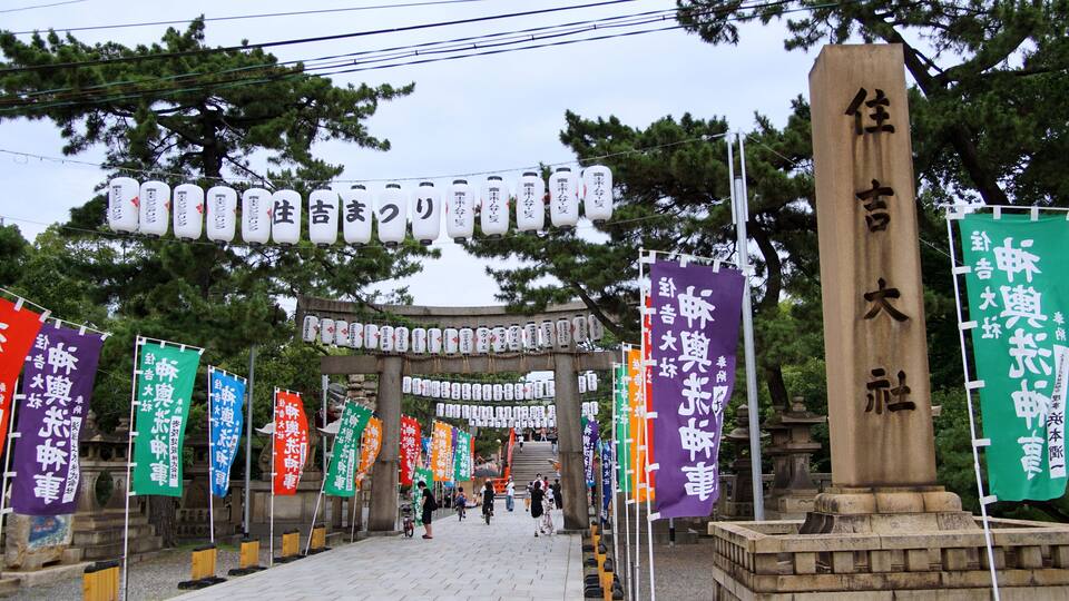 A traditional Japanese gate with multiple banners and a stone monument.