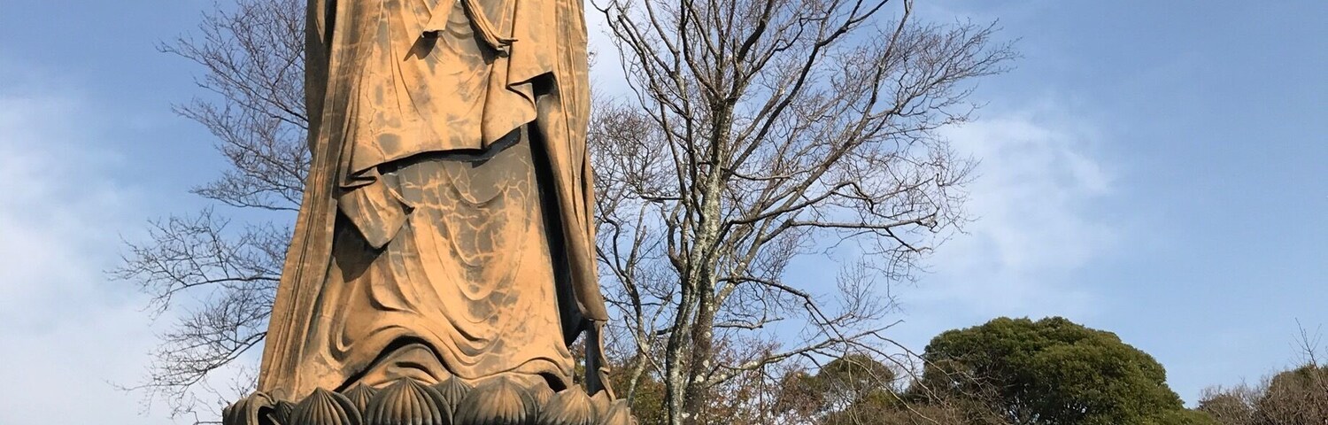 A large statue of a historical figure holding a staff, surrounded by traditional Chinese architectural elements and a clear blue sky.
