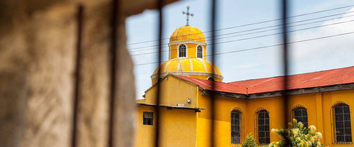 A yellow building with a red roof and a cross on top.