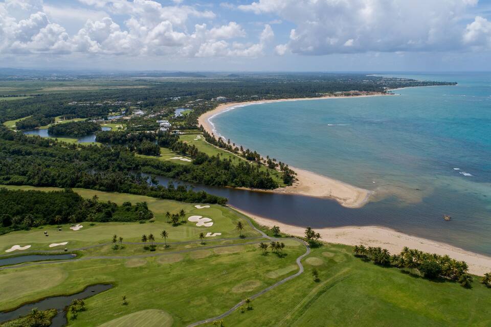 A coastal landscape with a golf course, a beach, and a bay.