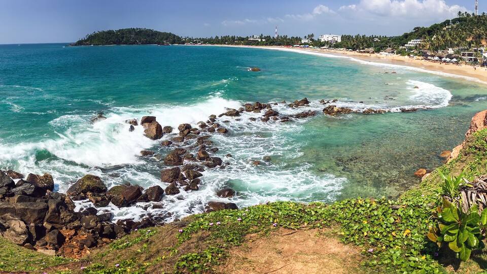 A coastal landscape with a rocky shoreline, clear turquoise waters, and a sandy beach.
