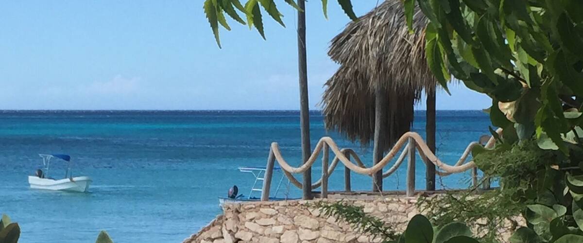A beach with a stone wall, a thatched-roof structure, and a boat in the water.