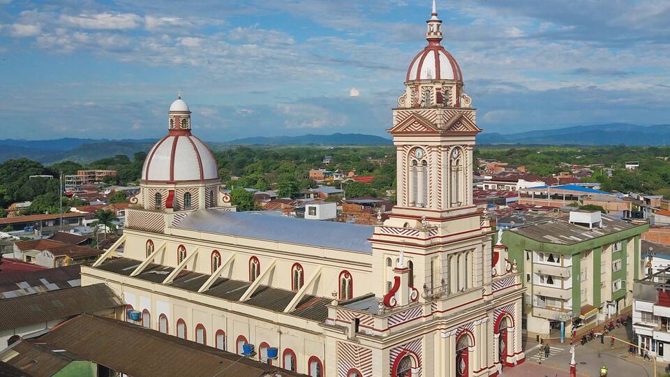 A large church with two domes and a bell tower, surrounded by a cityscape and mountains in the background.