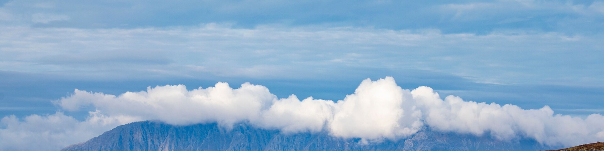 Una cordillera con un lago en primer plano y nubes arriba.
