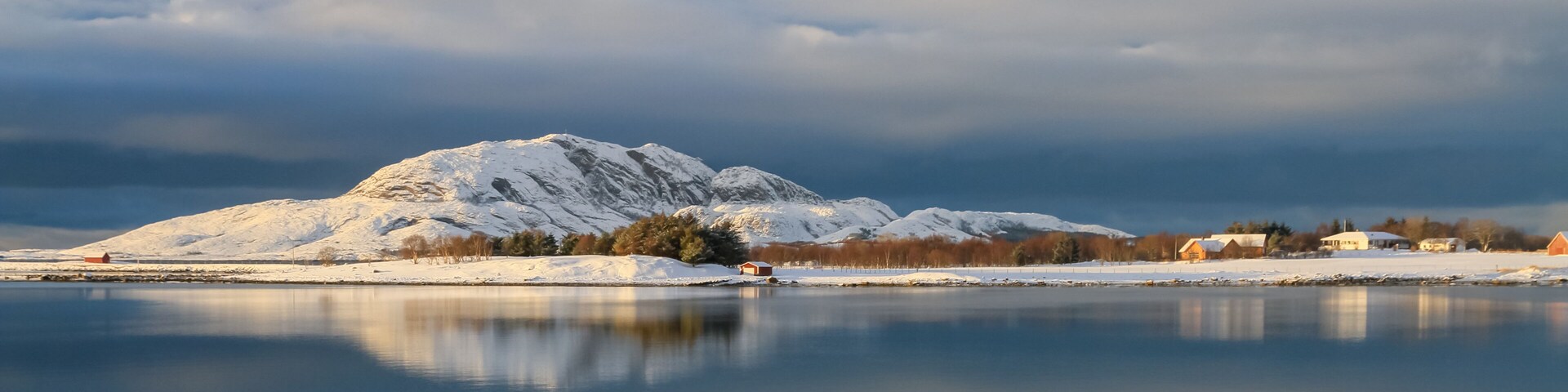 A snow-covered mountain, a calm lake, and a small village with buildings.