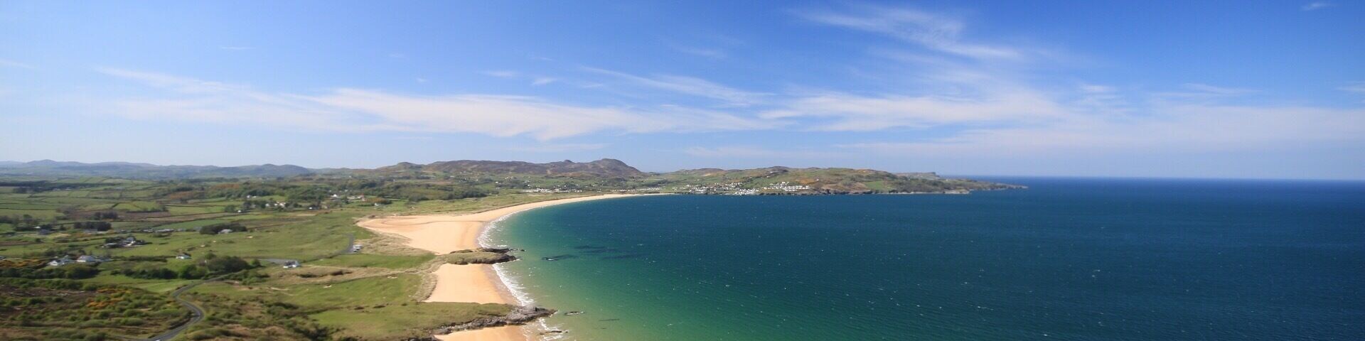 A coastal landscape with a sandy beach, green hills, and a clear blue sky.