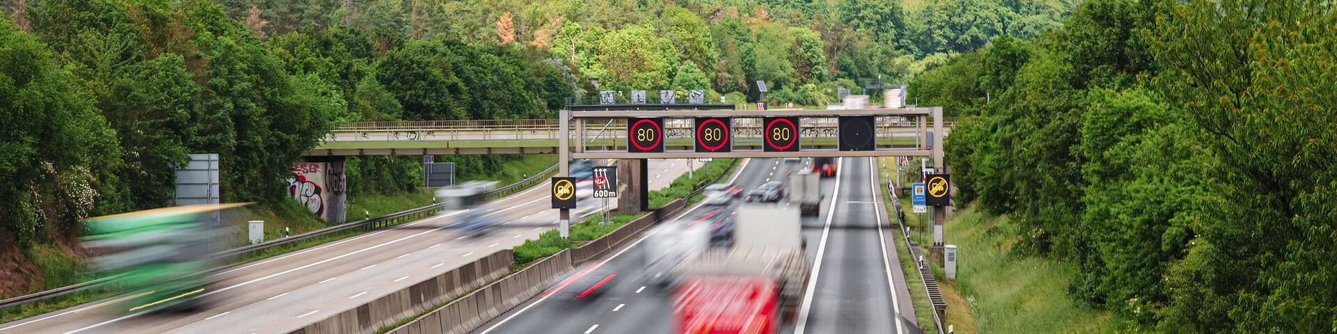 A highway with speed limit signs, a bridge, and a forested hillside in the background.