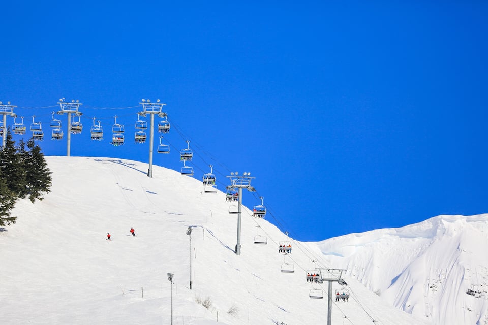 Un telefèric d'esquí en un vessant nevós de muntanya sota un cel blau clar.