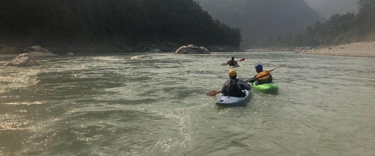 Kayakers on a river surrounded by forested mountains.