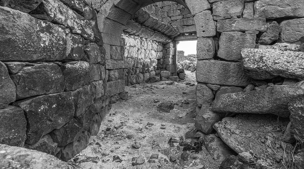 An ancient stone archway leading into a narrow passageway with rough, uneven stone walls and a dusty ground.