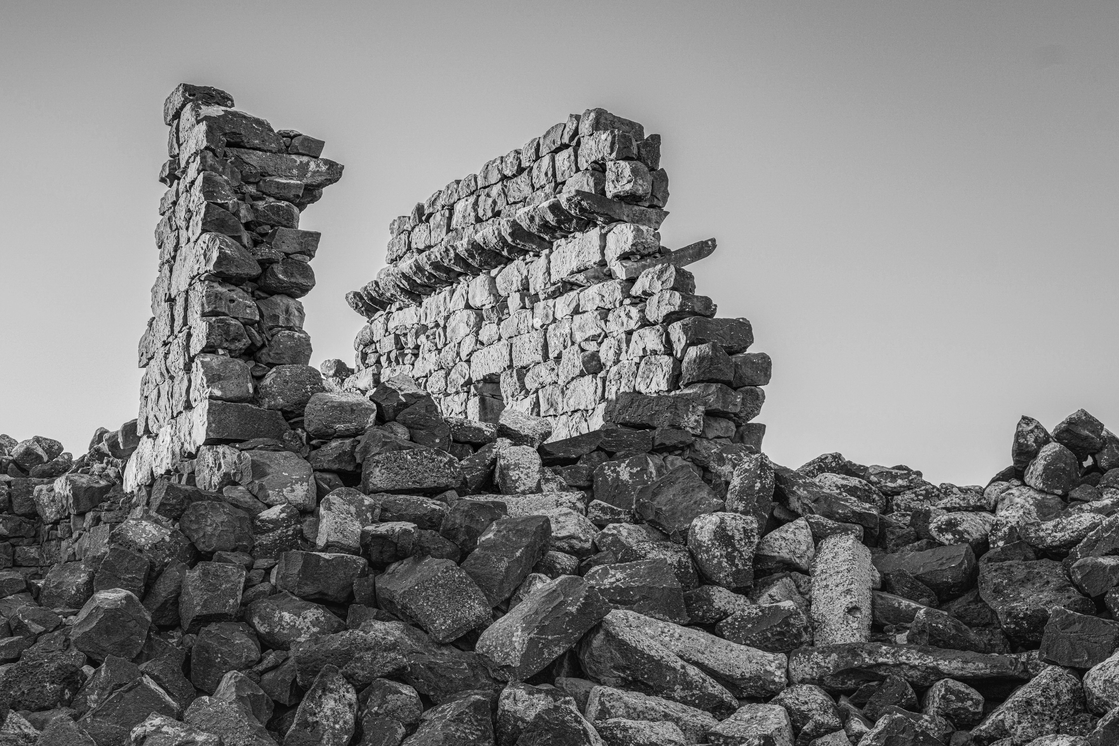 A black and white photograph of a collapsed stone structure amidst a pile of rubble.