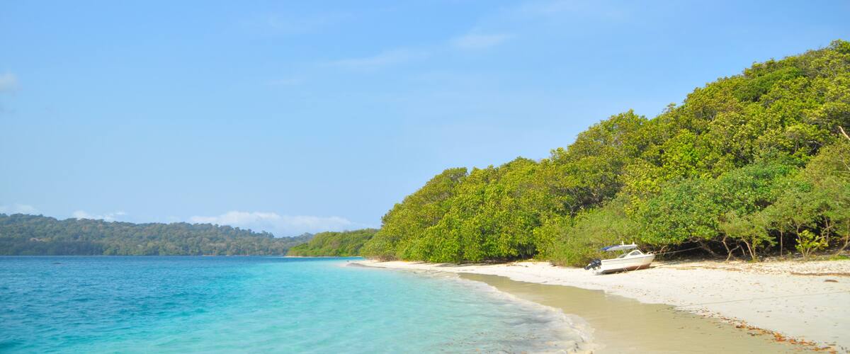 A beach with clear turquoise water, a sandy shore, and a boat on the beach.