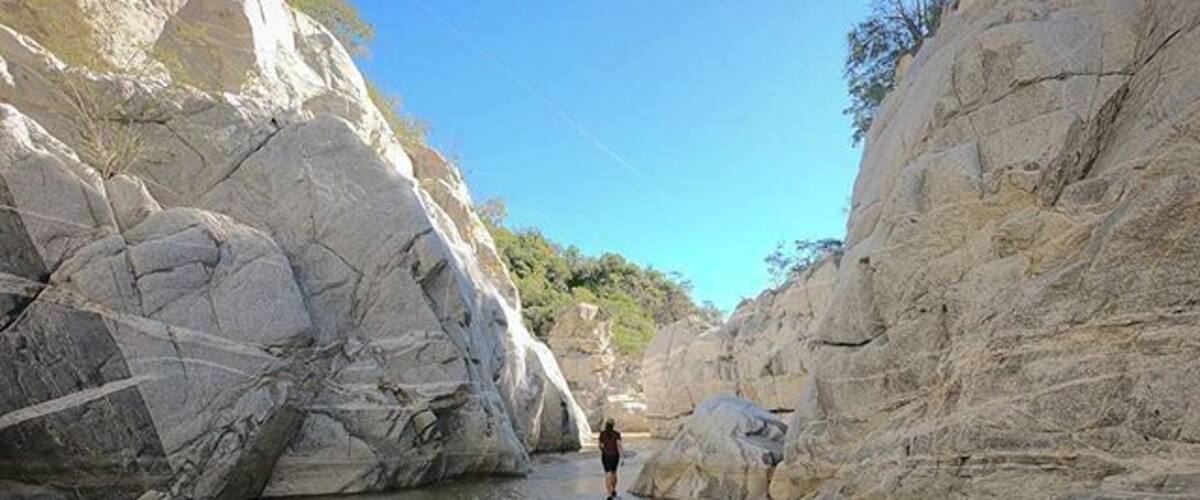 A narrow canyon with large boulders and a person standing in the middle.