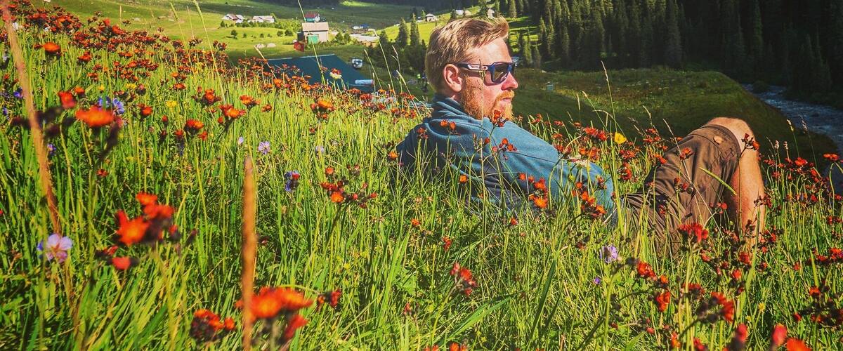 A person lying in a field of red poppies with mountains in the background.