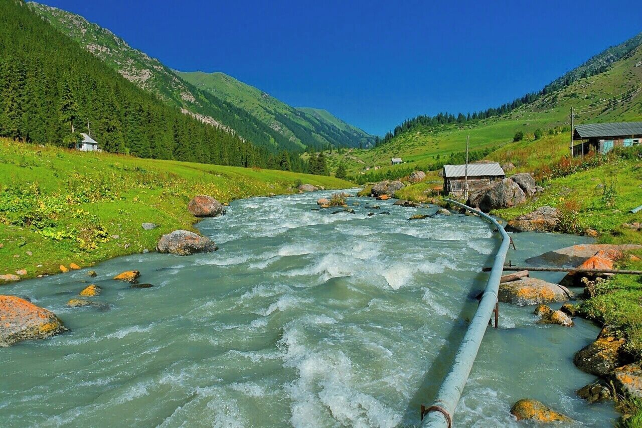 August 2013 
Altyn Arashan, Terskey Alatau, Tian Shan mountains, Kyrgyzstan 

View of Arashan river in the village of Altyn Arashan located in a lush valley where sheep and horses are herded by locals. The pipe is for hot water coming from near springs to concrete basins for relaxing bathing. The water is naturally very hot (45 degrees Celsius) and sulphuric. For equivalent of few dollars you can enjoy it anytime of the day. The water in the river is on the opposite very cold and wild even in summer months. This place is in altitude of 2.500 metres and some 4 hours of hike from Ak-su village near Karakol town. 