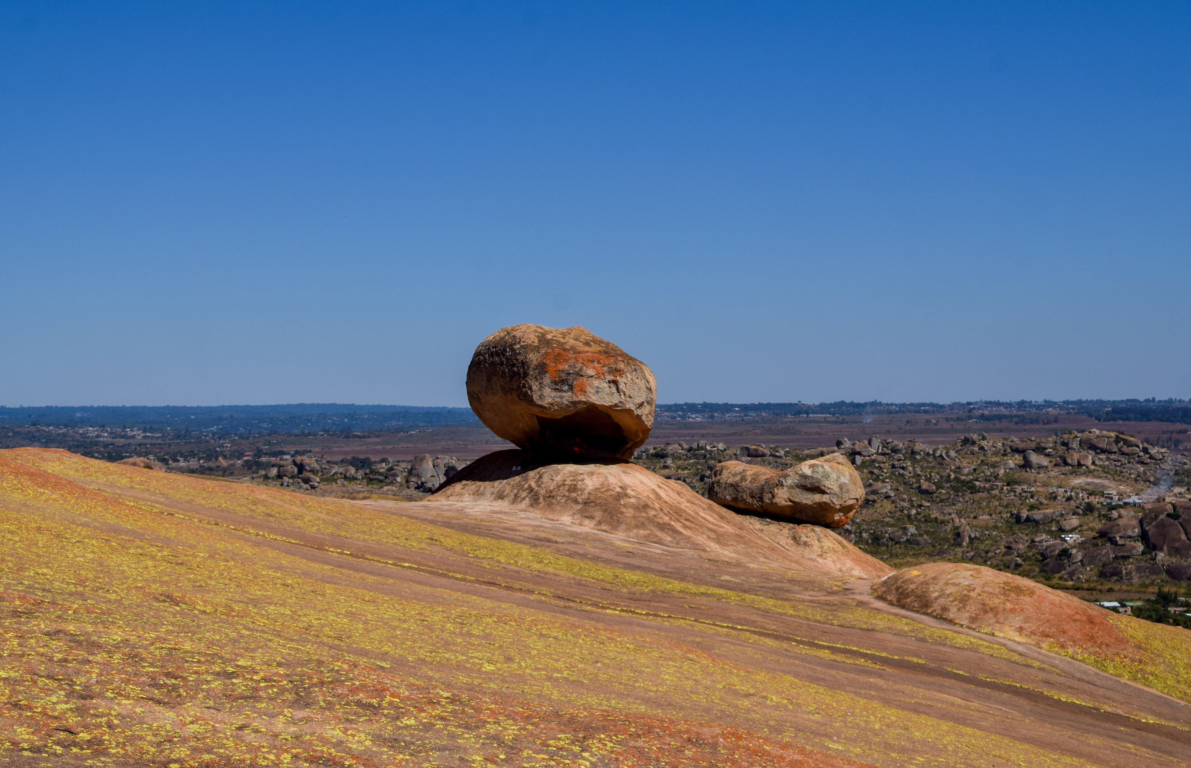 A large balanced rock formation on a hillside with a clear blue sky in the background.