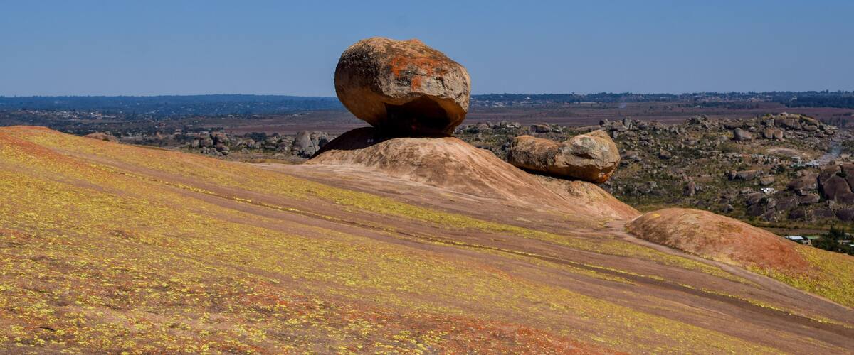 A large balanced rock formation on a hillside with a clear blue sky in the background.
